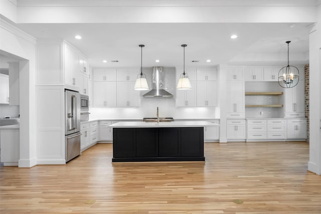 kitchen with appliances with stainless steel finishes, wall chimney exhaust hood, white cabinets, and light countertops