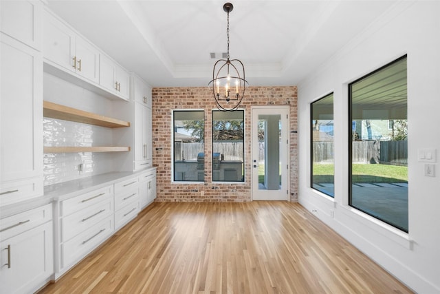 unfurnished dining area featuring a tray ceiling, a notable chandelier, brick wall, and light wood finished floors