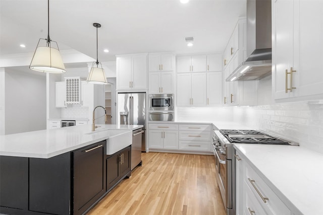 kitchen with wall chimney range hood, premium appliances, white cabinets, and a sink