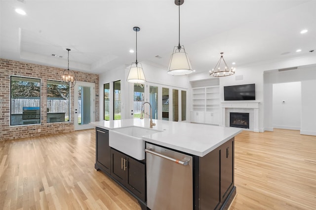 kitchen featuring a glass covered fireplace, a sink, stainless steel dishwasher, a notable chandelier, and open floor plan