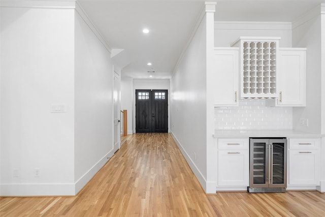 entrance foyer featuring beverage cooler, baseboards, light wood finished floors, a bar, and crown molding