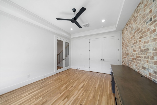 unfurnished bedroom with light wood finished floors, visible vents, brick wall, baseboards, and a raised ceiling