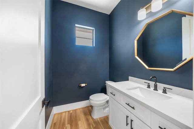 half bathroom with toilet, vanity, baseboards, and wood finished floors