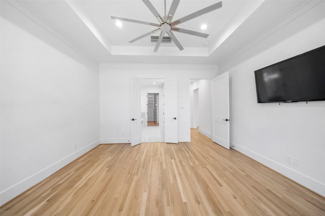 interior space with light wood-type flooring, a tray ceiling, baseboards, and ceiling fan