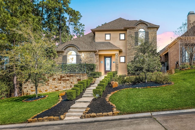 view of front of property with roof with shingles, a yard, and stucco siding