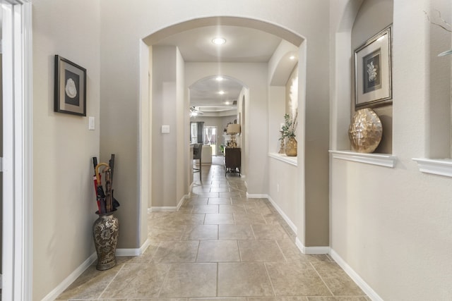 hall featuring arched walkways, light tile patterned floors, and baseboards