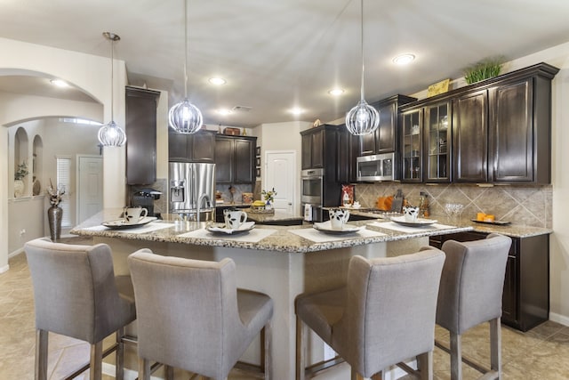 kitchen featuring a breakfast bar, light stone counters, arched walkways, appliances with stainless steel finishes, and dark brown cabinets