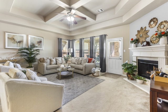 carpeted living area with visible vents, a fireplace with raised hearth, beamed ceiling, coffered ceiling, and a ceiling fan