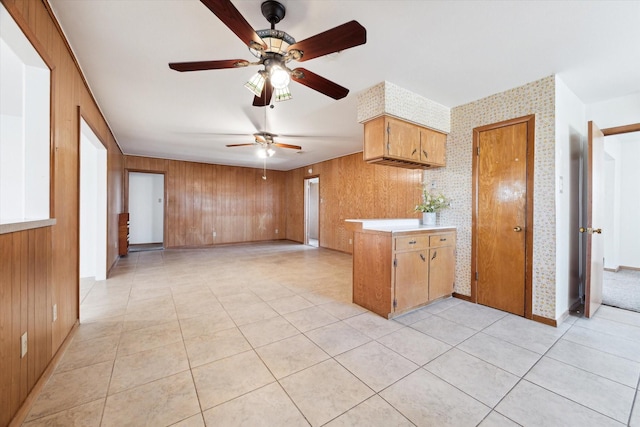 kitchen featuring light tile patterned floors, wooden walls, a ceiling fan, light countertops, and brown cabinets