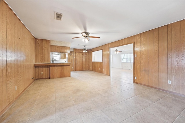 empty room with ceiling fan, wooden walls, visible vents, and light tile patterned flooring