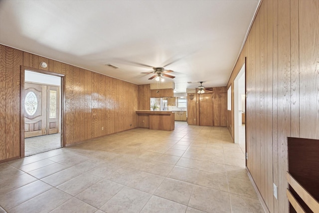 unfurnished living room featuring light tile patterned floors, wooden walls, visible vents, and a ceiling fan