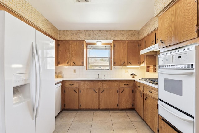 kitchen with a warming drawer, light countertops, white appliances, under cabinet range hood, and wallpapered walls