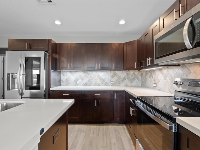 kitchen with dark brown cabinetry, tasteful backsplash, light wood-style flooring, appliances with stainless steel finishes, and light countertops