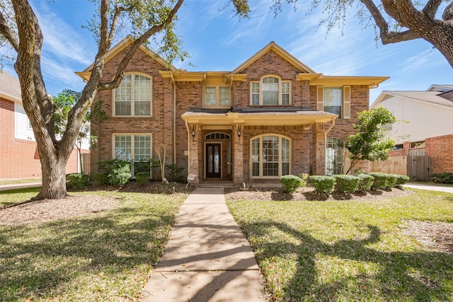 view of front of home with brick siding, a front lawn, and fence