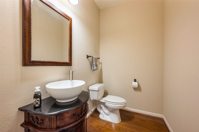 half bathroom with toilet, a sink, baseboards, and wood finished floors