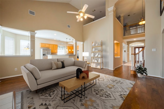 living area with arched walkways, visible vents, baseboards, wood-type flooring, and ornate columns