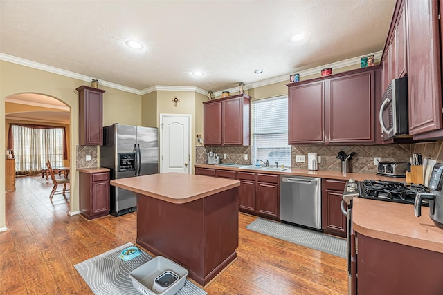 kitchen with light wood-style floors, appliances with stainless steel finishes, arched walkways, and light countertops