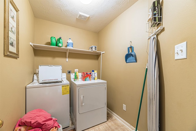 washroom with a textured ceiling, laundry area, visible vents, baseboards, and washer and dryer