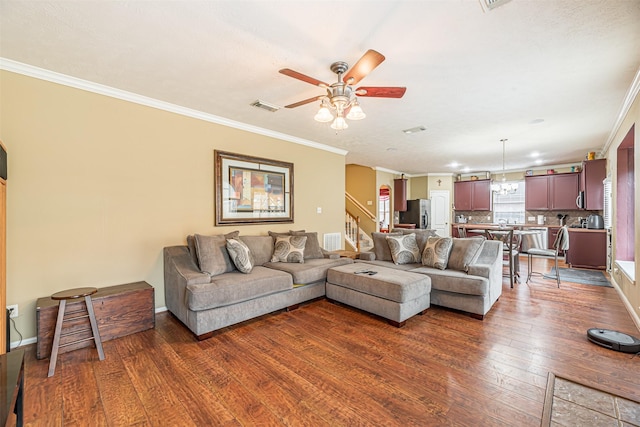 living area featuring dark wood-style floors, crown molding, ceiling fan with notable chandelier, visible vents, and stairs