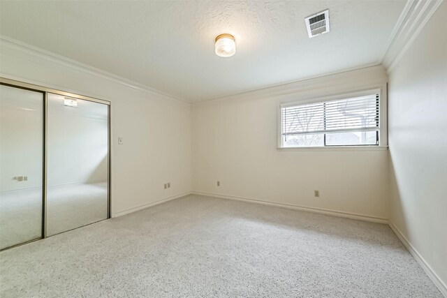 unfurnished bedroom featuring baseboards, visible vents, a textured ceiling, crown molding, and a closet