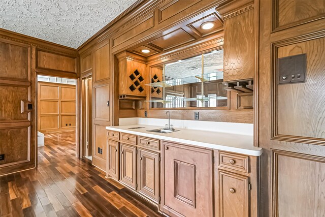 kitchen with wooden walls, dark wood-style flooring, a sink, light countertops, and crown molding