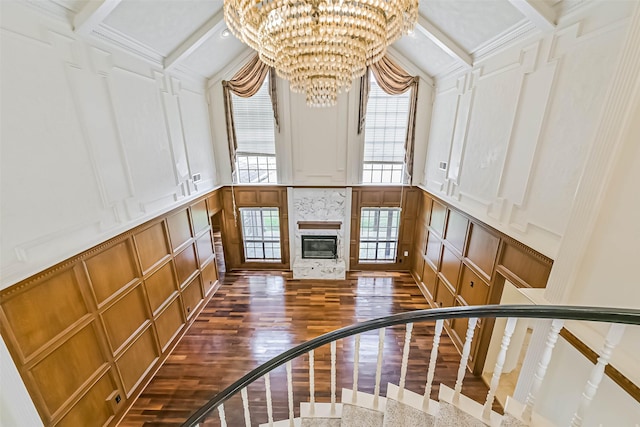 unfurnished living room featuring a decorative wall, an inviting chandelier, a tile fireplace, beam ceiling, and dark wood-style floors