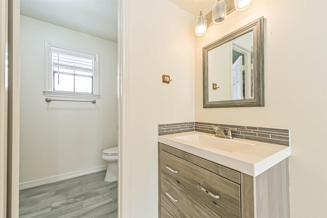 bathroom with toilet, wood finished floors, vanity, baseboards, and decorative backsplash