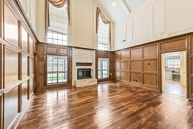 unfurnished living room with a wealth of natural light, dark wood finished floors, a high end fireplace, and a decorative wall