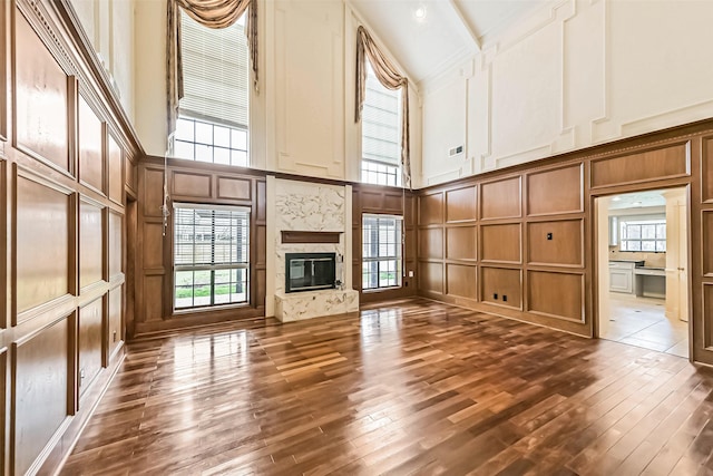 unfurnished living room with a premium fireplace, a towering ceiling, dark wood finished floors, and a decorative wall