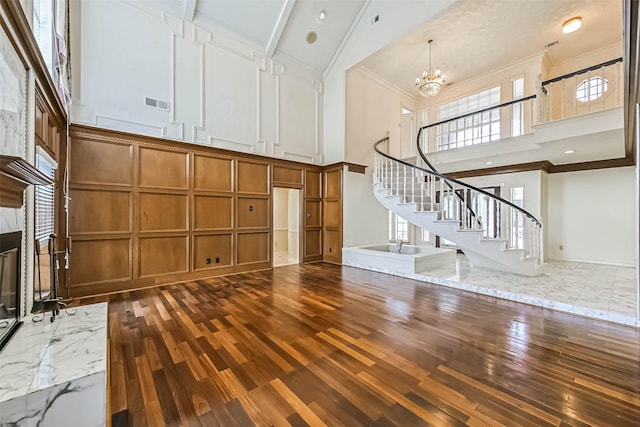 unfurnished living room with stairway, a decorative wall, crown molding, a high ceiling, and a notable chandelier
