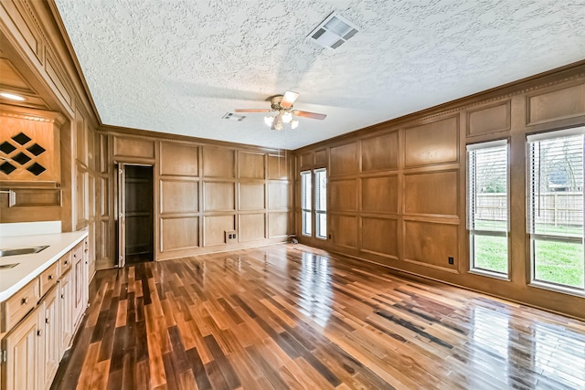 unfurnished living room featuring crown molding, visible vents, a decorative wall, and dark wood-style floors