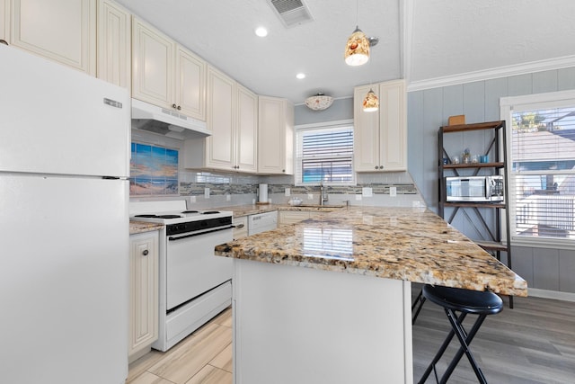 kitchen featuring visible vents, decorative backsplash, white appliances, under cabinet range hood, and a kitchen bar