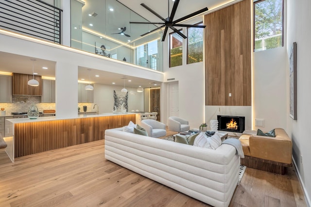 living room featuring a fireplace, light wood finished floors, visible vents, a towering ceiling, and a ceiling fan