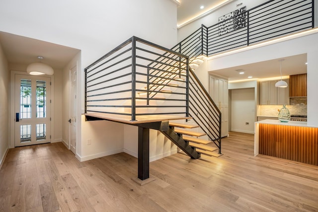 entryway with stairs, a towering ceiling, light wood-style flooring, and baseboards