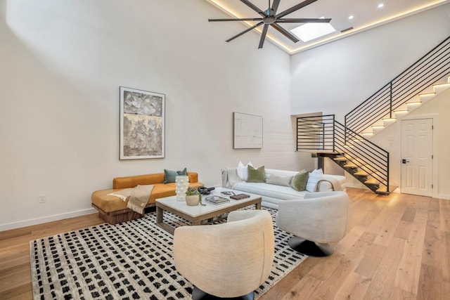 living area featuring a skylight, baseboards, stairs, a high ceiling, and light wood-style floors