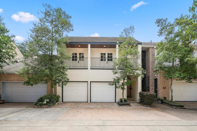 front facade featuring a balcony, driveway, an attached garage, and brick siding