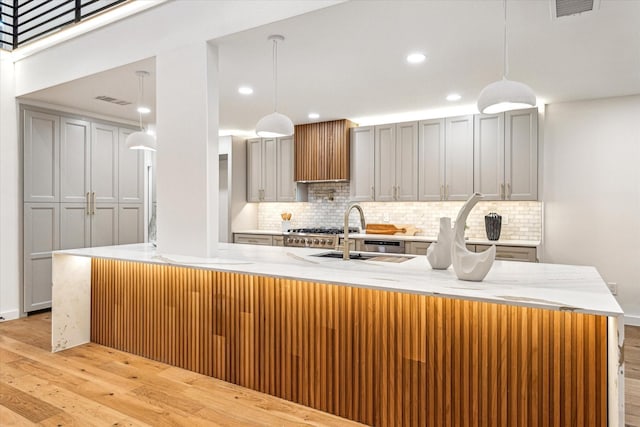 kitchen featuring tasteful backsplash, visible vents, light wood-style flooring, custom exhaust hood, and a sink