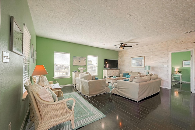 living room with wood-type flooring, visible vents, wood walls, ceiling fan, and a textured ceiling