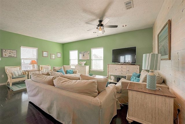 living room featuring a textured ceiling, dark wood-style flooring, visible vents, baseboards, and a ceiling fan