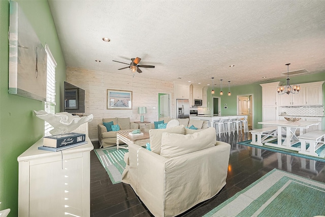 living area with a textured ceiling, visible vents, dark wood-type flooring, and ceiling fan with notable chandelier