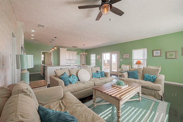 living area with baseboards, visible vents, a textured ceiling, and ceiling fan with notable chandelier