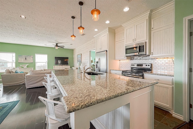 kitchen featuring a breakfast bar area, stainless steel appliances, tasteful backsplash, open floor plan, and a sink