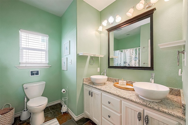 bathroom with double vanity, a sink, toilet, and baseboards