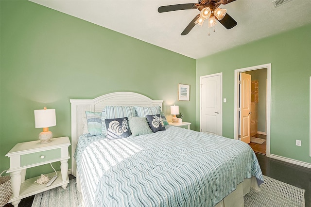 bedroom with ceiling fan, wood finished floors, visible vents, baseboards, and ensuite bath