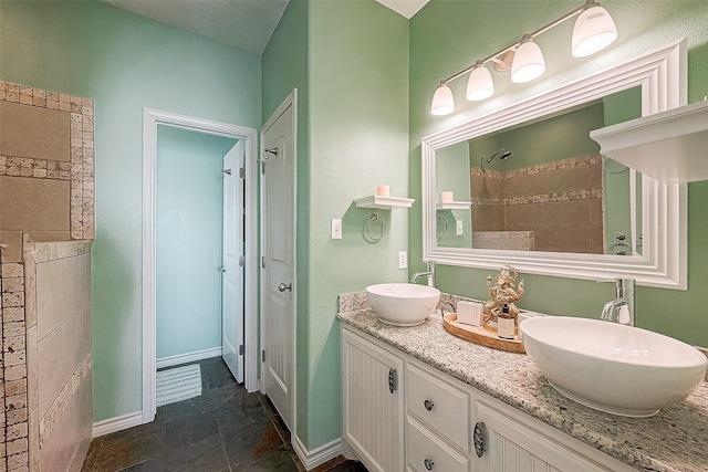 full bath featuring tiled shower, a sink, baseboards, and double vanity