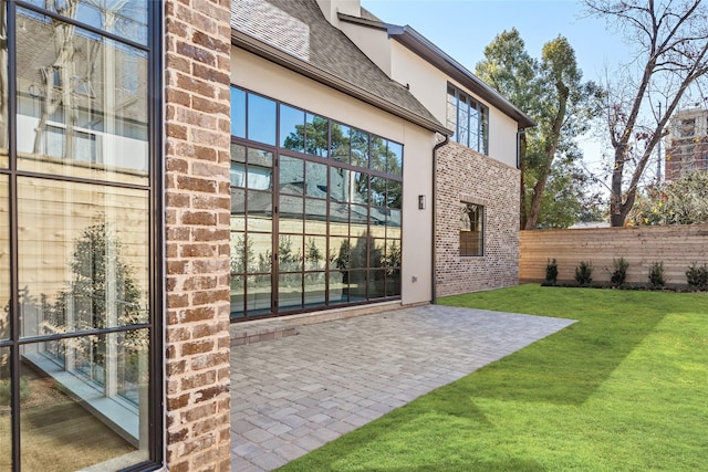 view of exterior entry with brick siding, a lawn, a patio, fence, and stucco siding