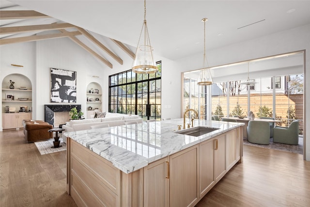 kitchen featuring built in features, open floor plan, light brown cabinets, a sink, and wood finished floors