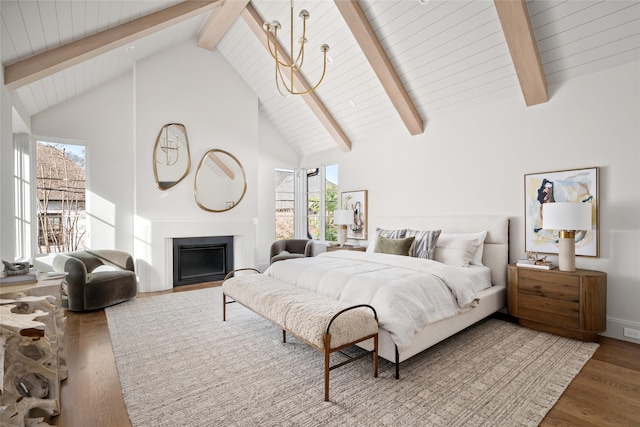 bedroom with high vaulted ceiling, beamed ceiling, a fireplace, and wood finished floors