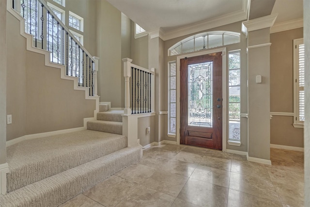 entrance foyer featuring baseboards, crown molding, a towering ceiling, and ornate columns