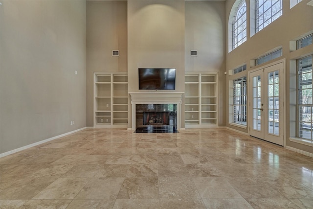 unfurnished living room with french doors, visible vents, a high ceiling, a tiled fireplace, and baseboards